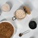 Top view of various grains and seeds in bowls and jars on a white surface.